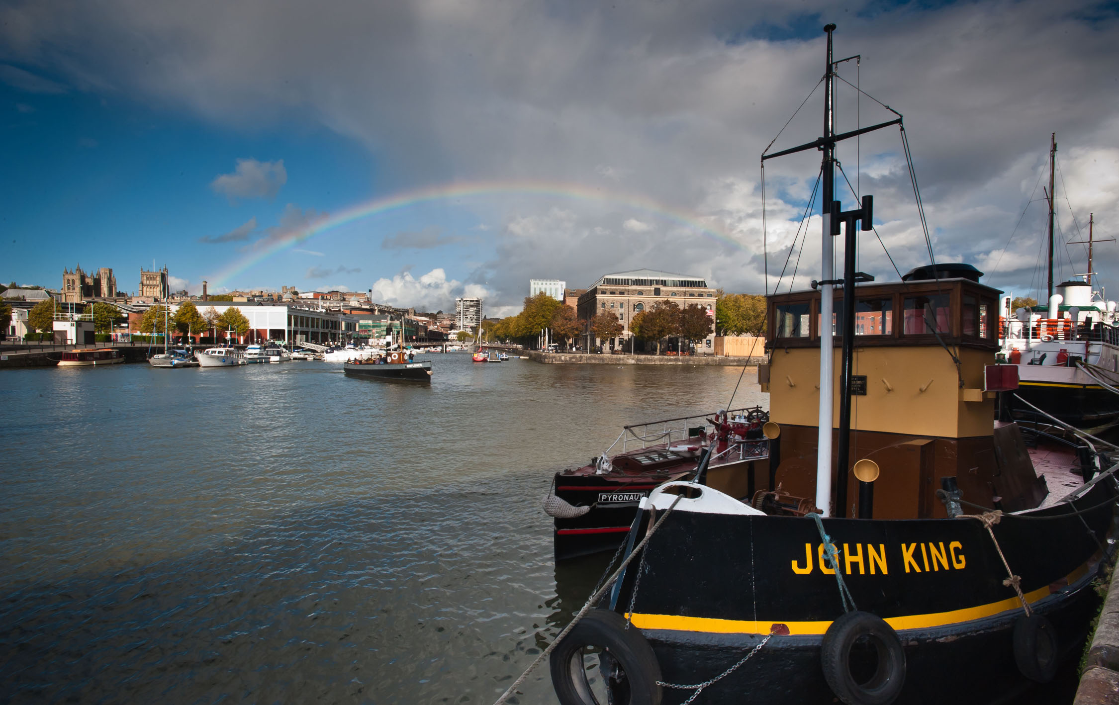 black boat with yellow writing on the river with a rainbow in the background