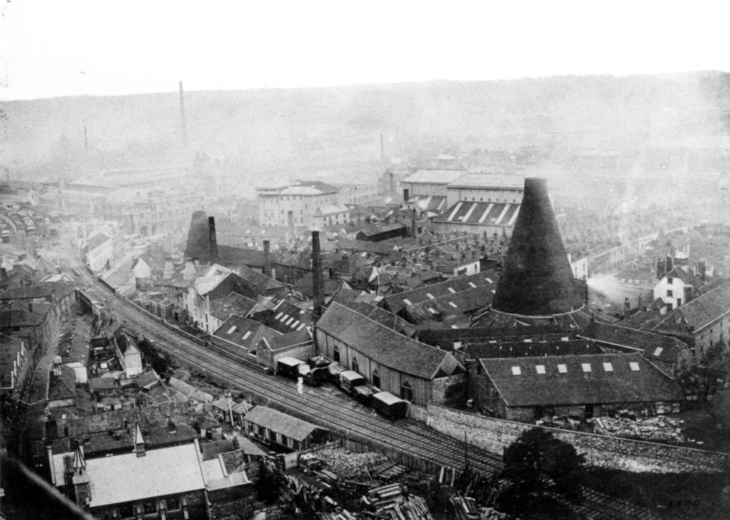 black and white aerial view of a train track going between buildings