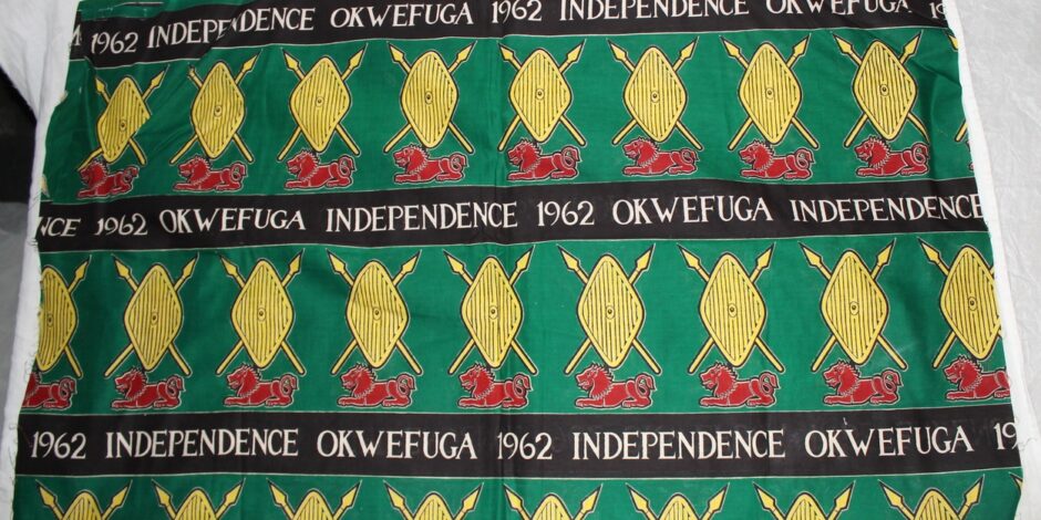 green red and yellow textile celebrating Ugandan independence. There is a black banner that runs across it with words stating " Okwefuga Independence 1962"